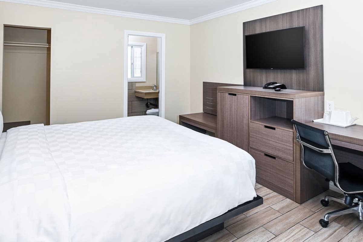 A hotel room with a bed, a desk, a chair, a TV, and a bathroom.