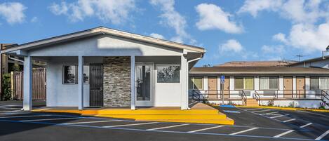 Un motel con estacionamiento techado, entrada con portón y señal de acceso para sillas de ruedas.