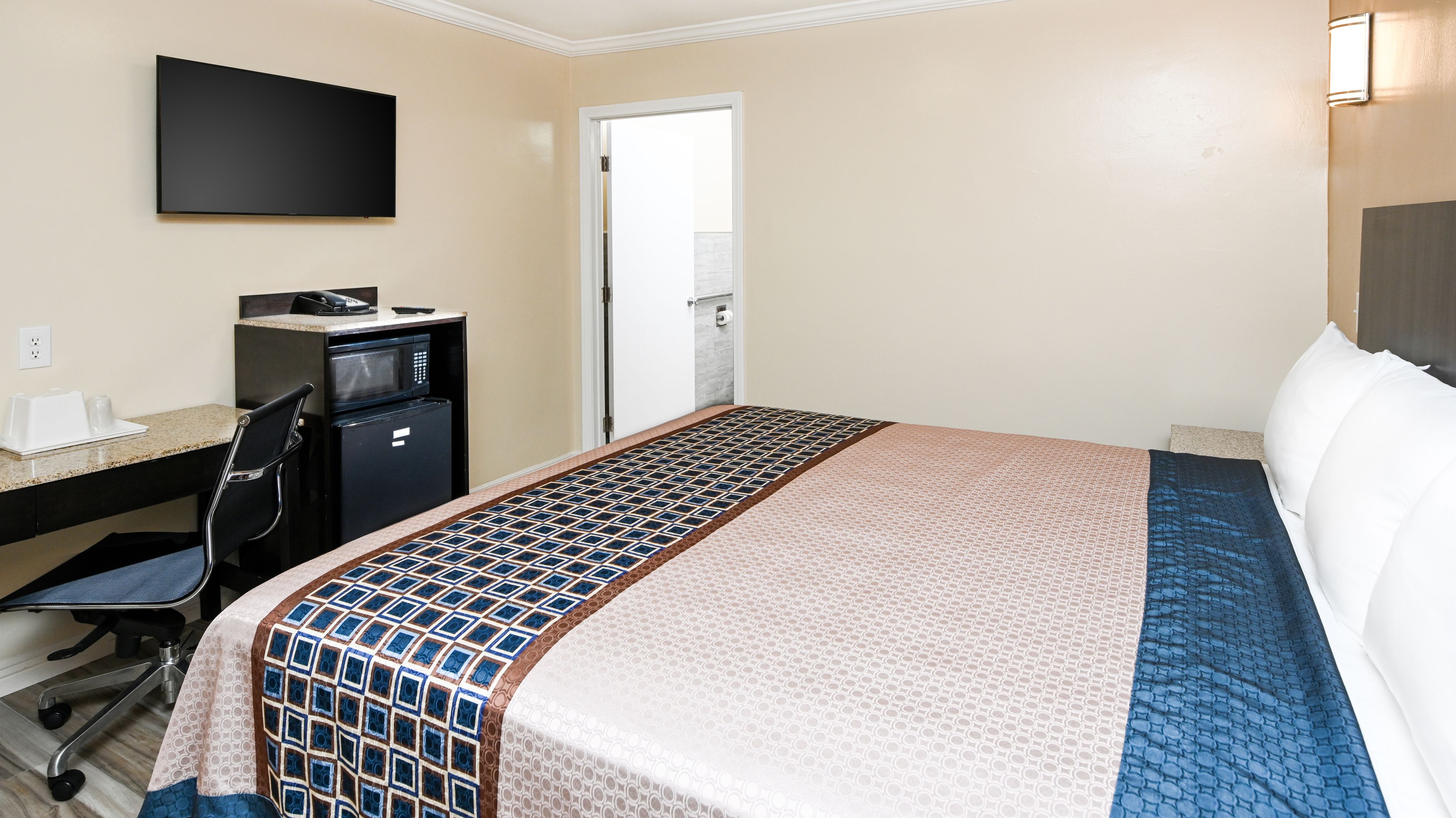 Ein Hotelzimmer mit einem Bett, einem Schreibtisch mit Computer, einer Mikrowelle und einem Fernseher.