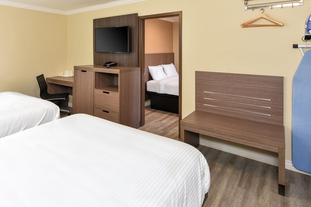 A hotel room with two beds, a desk with a chair, a TV mounted on the wall, and a wardrobe.
