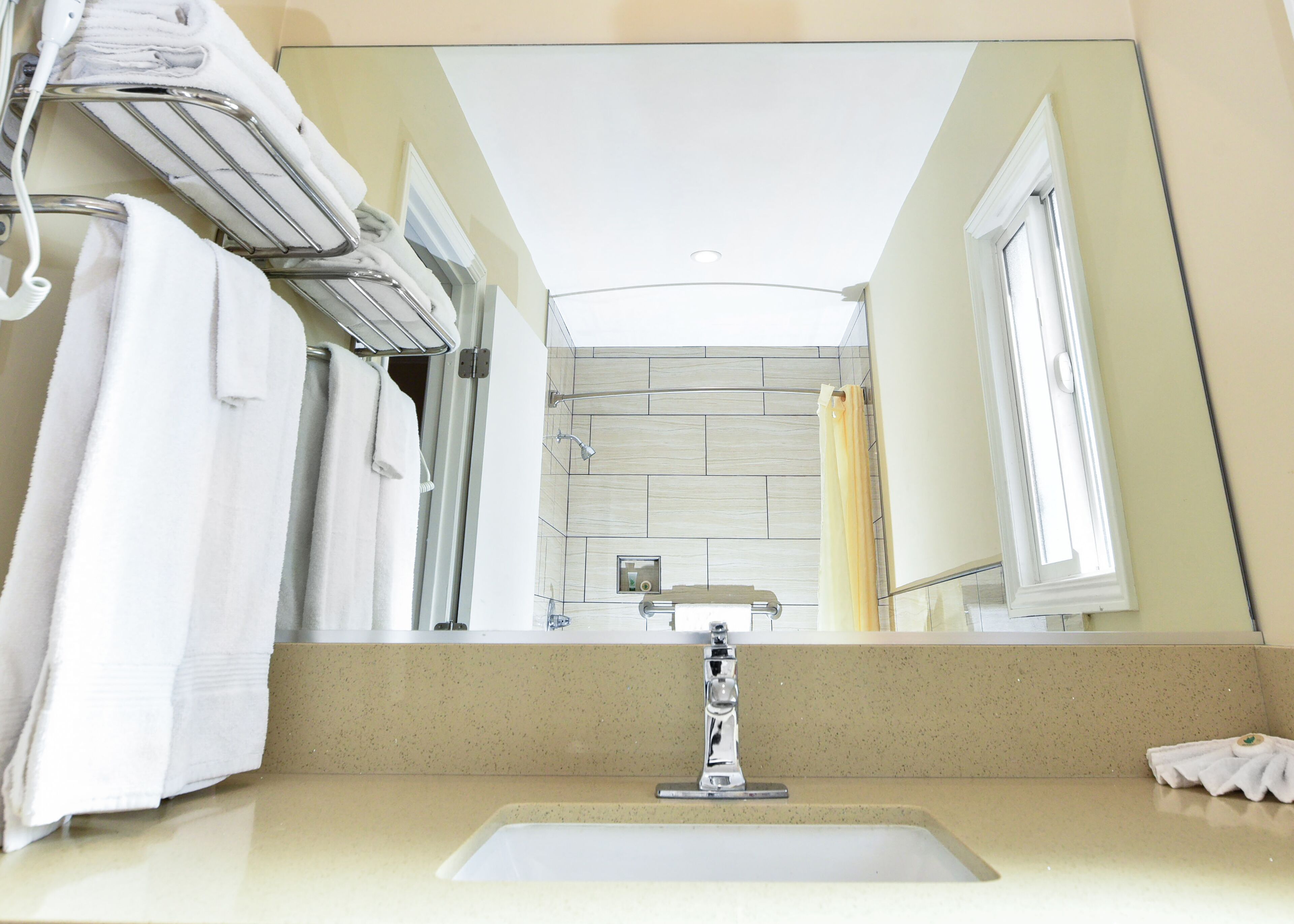 A bathroom with a large mirror, a sink, and a towel rack.