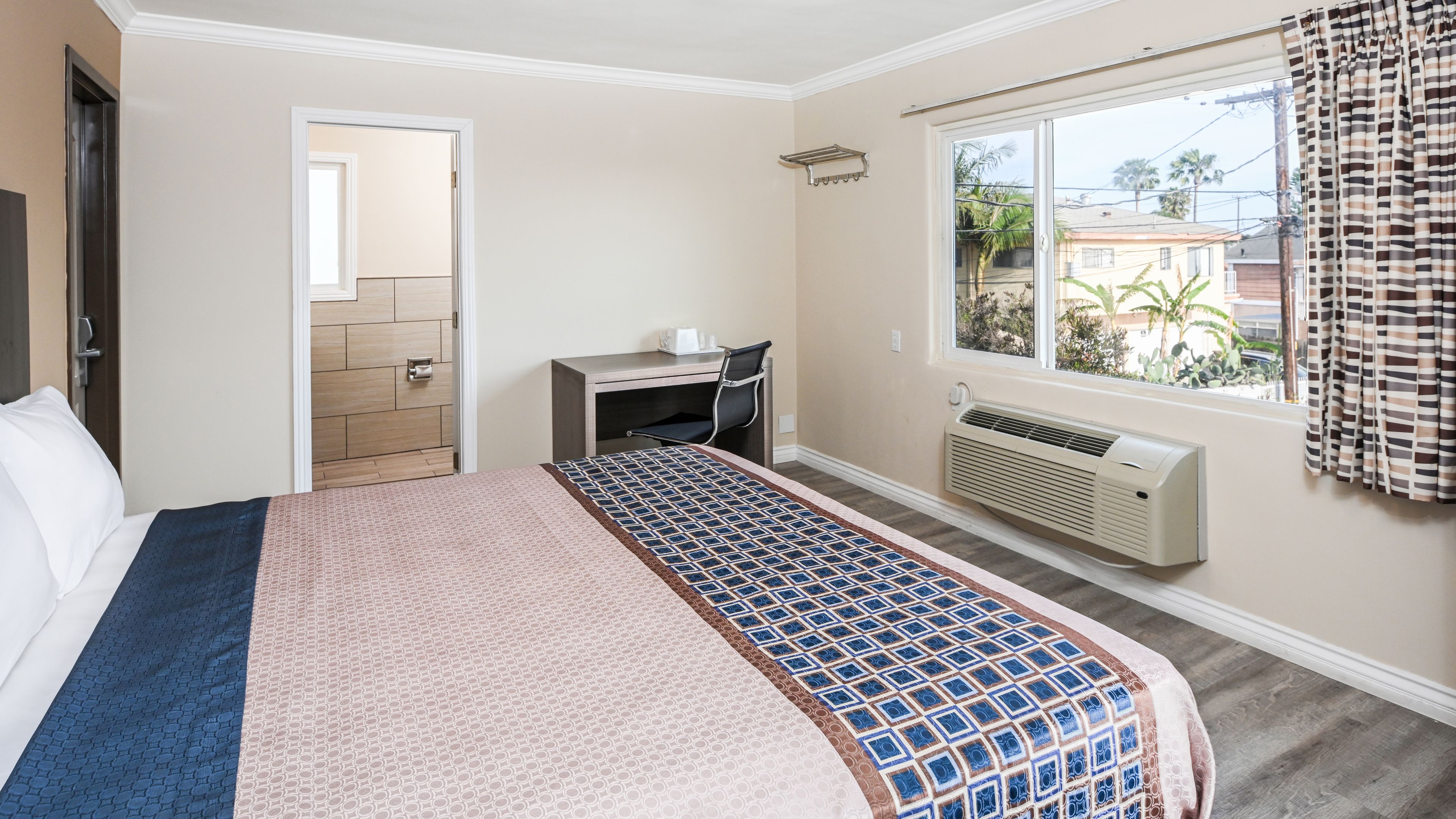 A hotel room with a bed, a desk, a window with curtains, and a view of the outside.