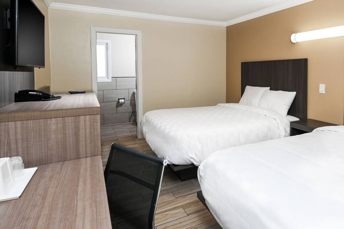 A hotel room with two beds, a desk, a chair, a telephone, and a mirror.