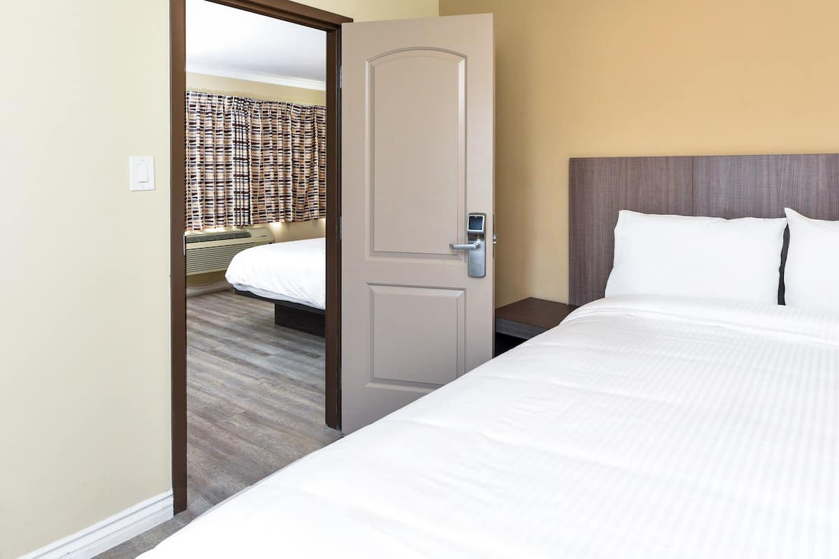 A hotel room with a bed, a door, and a wall with a patterned curtain.