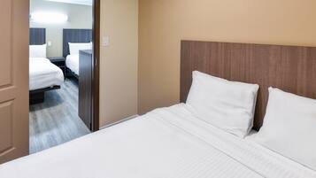 A hotel room with a large bed, a wooden headboard, and a view into the adjacent room.