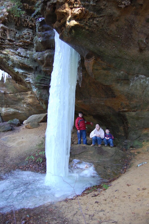 A waterfall cascading into a rocky cave with three people standing and sitting nearby.