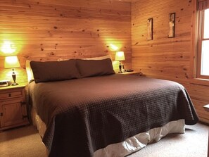 Un dormitorio con paneles de madera, una cama grande, dos lámparas de noche y una mesita de noche.