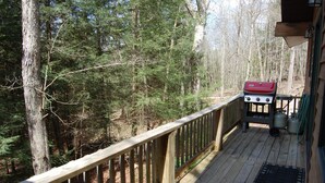 A wooden deck with a barbecue grill and propane tanks, surrounded by a forest.
