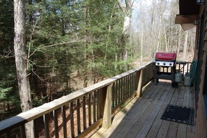 Une terrasse en bois équipée d’un barbecue et de bouteilles de propane, entourée d’une forêt.