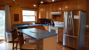A kitchen with wooden cabinets, a stainless steel refrigerator, a microwave, and a sink. There are two wooden chairs and a small island with a countertop.