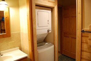 Une buanderie équipée d’un lave-linge et d’un sèche-linge, avec une porte en bois et un évier surmonté d’un miroir.
