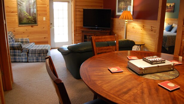 A cozy cabin interior with a wooden interior, a television, a dining table with a red book, and a sofa.