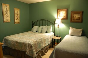 Une chambre à coucher avec un lit, une table de chevet, une lampe et deux tableaux encadrés accrochés au mur.
