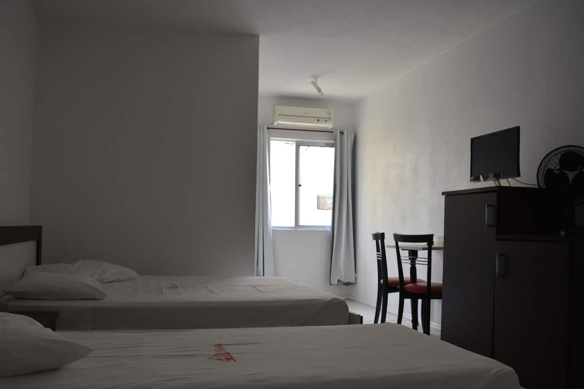 Habitación de hotel con dos camas individuales, un escritorio con silla, televisor y aire acondicionado.