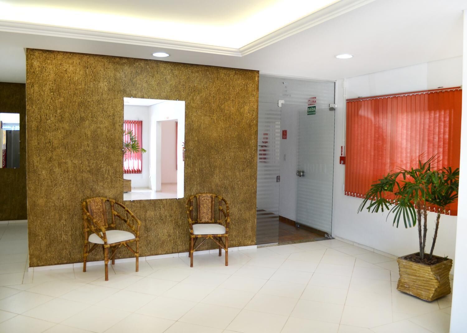 A reception area with two wicker chairs, a large mirror, a potted plant, and a red curtain.