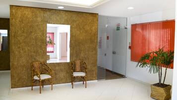 A reception area with two wicker chairs, a large mirror, a potted plant, and a red curtain.