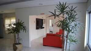 A living room with a red sofa, a flat-screen TV mounted on the wall, and two potted plants. - Arpini Hotel (Rio Grande)