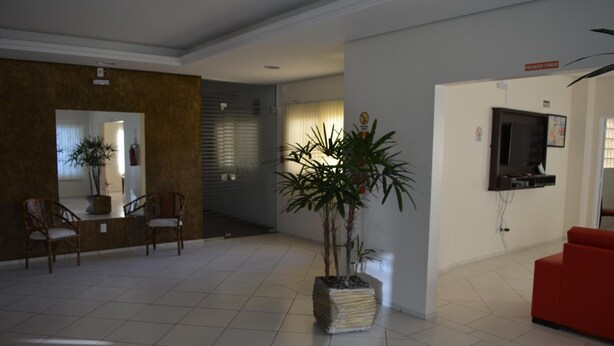 A spacious living area with a tiled floor, a red sofa, two wooden chairs, and a large potted plant. - Arpini Hotel (Rio Grande)