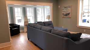 A modern living room with a large grey sectional sofa, a small black armchair, and a window with a view of a building. - Location, Location, Location! Downtown Newport! Newly Renovated (Newport)