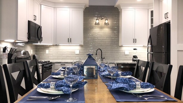 A modern kitchen with white cabinets, a black refrigerator, and a dining area set for six with blue placemats and wine glasses. - Location, Location, Location! Downtown Newport! Newly Renovated (Newport)