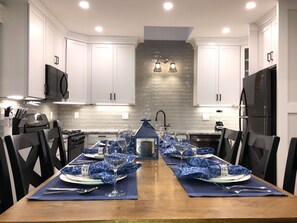 A modern kitchen with white cabinets, a black refrigerator, and a dining area set for six with blue placemats and wine glasses.