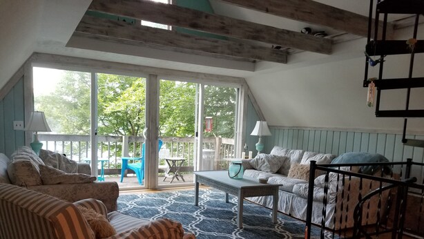 Una sala de estar acogedora con un sofá, un sillón y una mesita de centro. Hay un balcón con vistas a árboles.