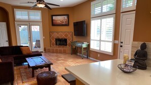 A living room with a sofa, coffee table, ottoman, fireplace, TV, Buddha statue, and a small table with candles and a book. - Relaxing Desert Oasis-Salt Water Pool & Jacuzzi/Mountain Views/#067735 3bd (La Quinta)