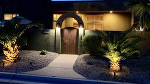 A residential building with a wooden front door, a driveway, and a well-maintained garden with palm trees. - Relaxing Desert Oasis-Salt Water Pool & Jacuzzi/Mountain Views/#067735 3bd (La Quinta)
