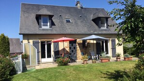 Ein zweistöckiges Haus mit überdachter Terrasse, einer Steinmauer und einem gepflegten Rasen.