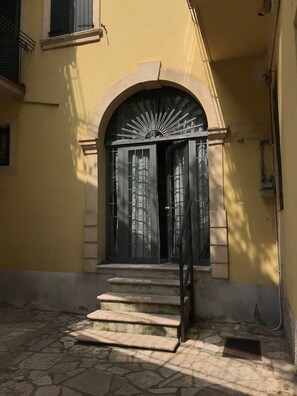 A building entrance with a stone staircase leading up to a black door with a sunburst design.