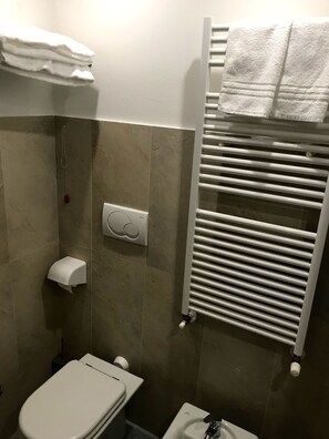 A bathroom with a toilet, bidet, towel rack, and a towel warmer.