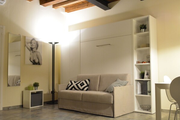 A modern living room with a beige sofa, a floor lamp, a bookshelf, and a mirror.