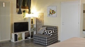 Uma sala de estar moderna com uma TV de tela plana sobre um suporte branco, uma poltrona estampada, parede de tijolos e uma porta.