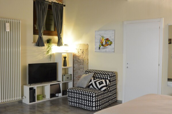 A modern living room with a flat-screen TV on a white stand, a patterned armchair, a brick accent wall, and a door.