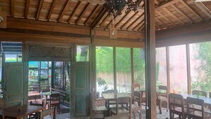 Un comedor interior con mesas y sillas de madera, ventanas amplias y techo de madera.