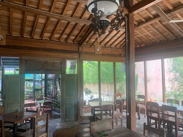 An indoor dining area with wooden tables and chairs, large windows, and a wooden ceiling.