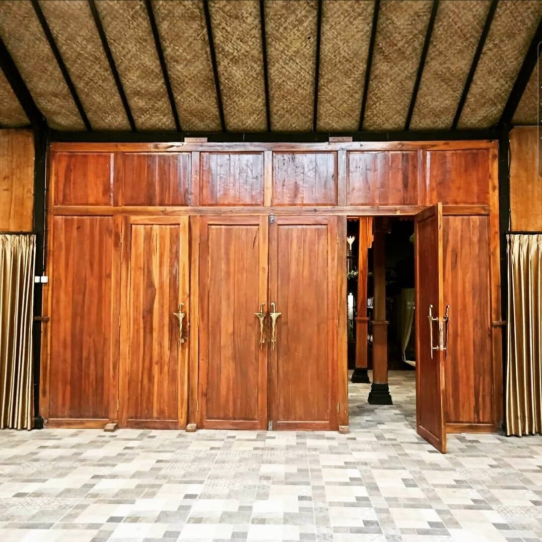 A room with a large wooden wardrobe, a checkered floor, and a thatched ceiling.