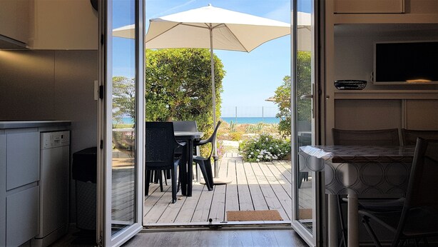 Una cocina con puerta de vidrio corrediza que da a un patio exterior con mesa y sillas, un gran paraguas y vista al océano.