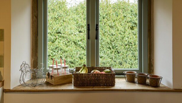 A window with a view of greenery, a wooden tray with jars and straws, and a wicker basket with fruits. - Cotswolds Barn Apartment - luxury self catering near Bath & Bristo (Bristol)
