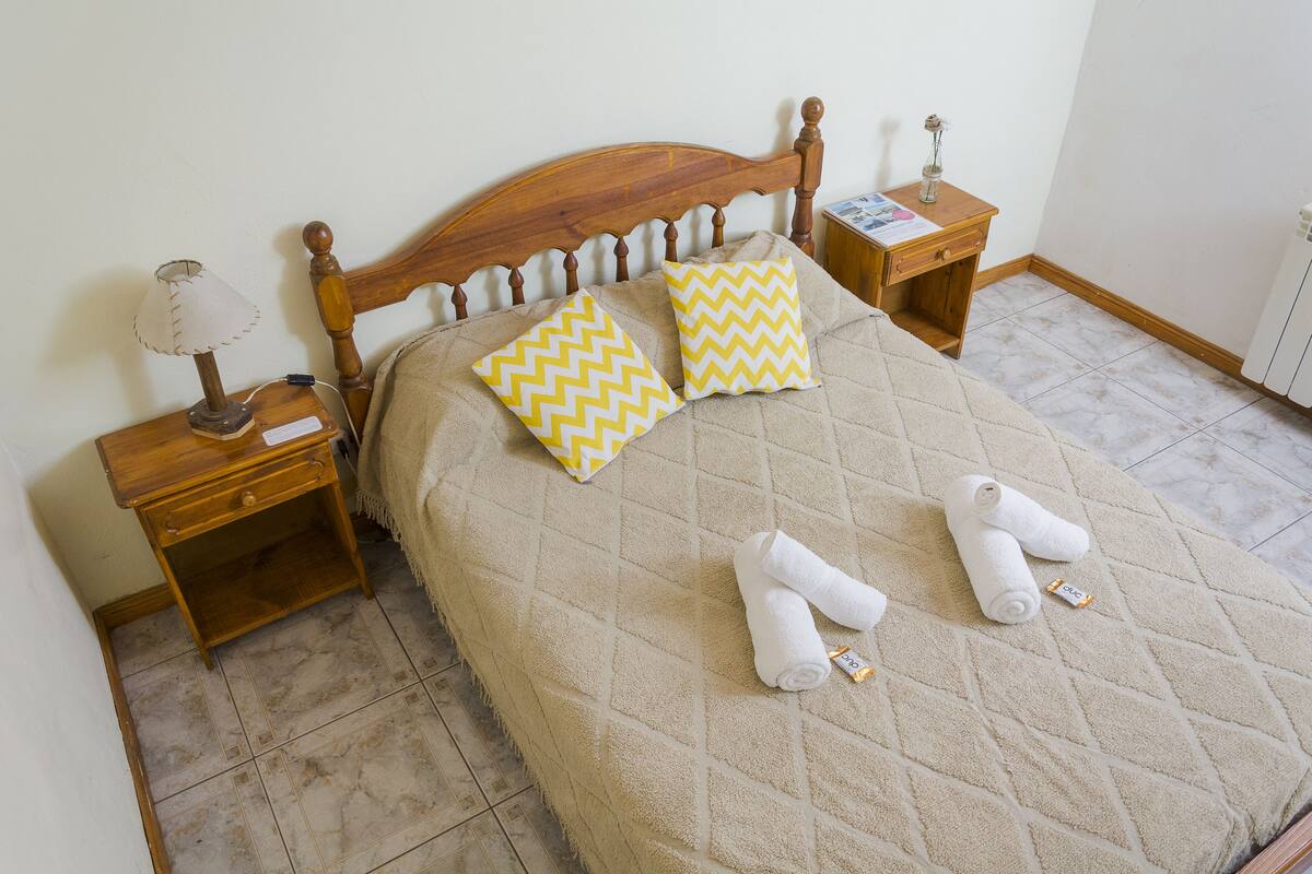 A neatly made bed with a quilted cover, two pillows with a chevron pattern, and two rolled towels on the bed.