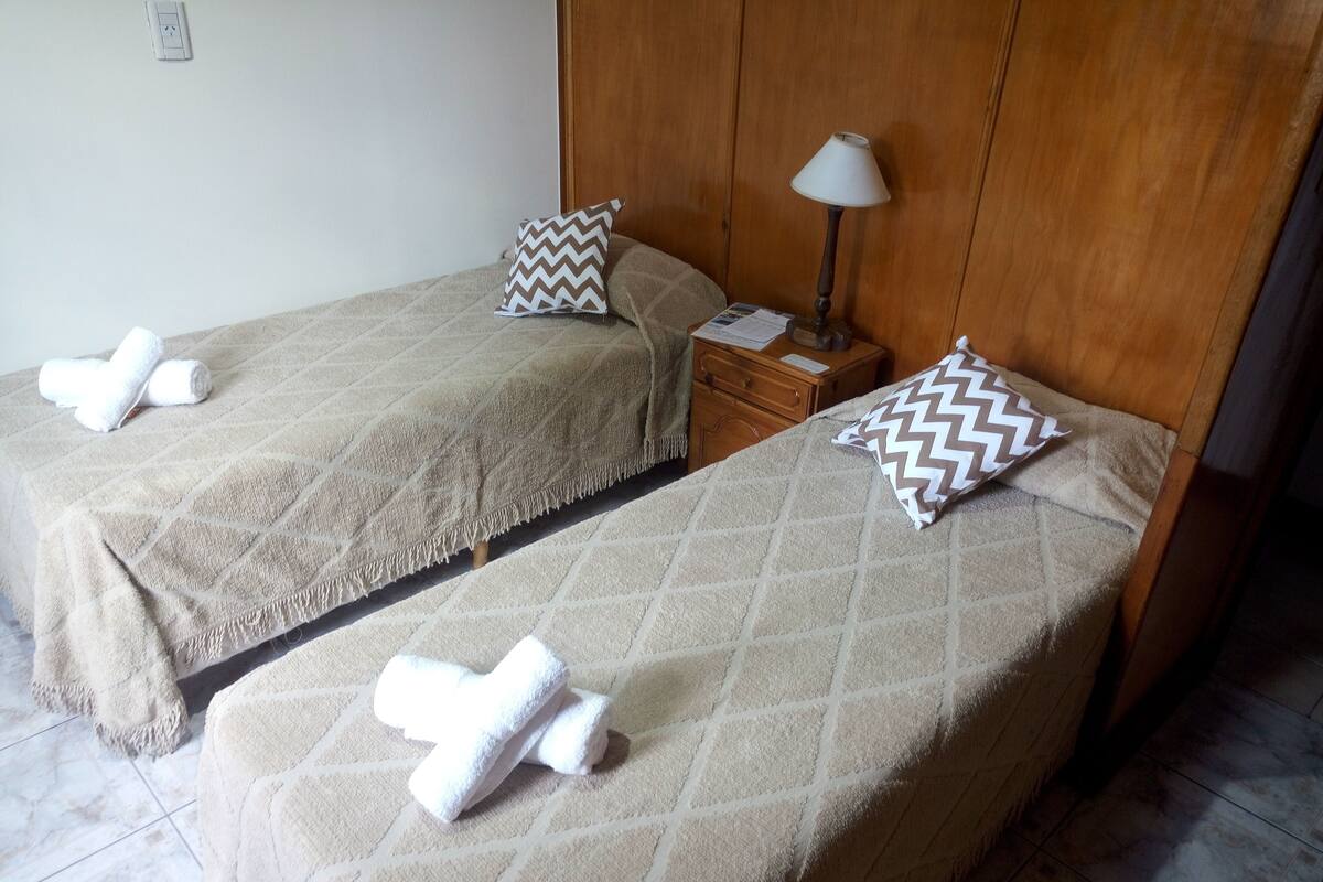 Two single beds with matching headboards, a bedside table with a lamp, and towels on each bed.