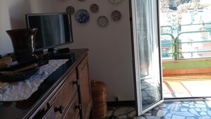 A room with a tiled floor, a wooden dresser, a television, and a wall decorated with various plates. - Wide View Apartment (Rapallo)