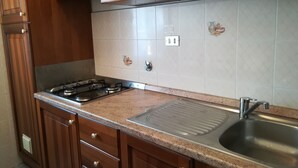 A kitchen with wooden cabinets, a gas stove, a stainless steel sink, and a tiled backsplash. - Wide View Apartment (Rapallo)