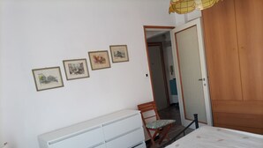 A bedroom with a bed, a wooden wardrobe, a white dresser, a chair, and four framed pictures on the wall. - Wide View Apartment (Rapallo)