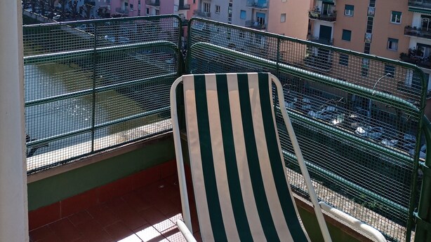 A balcony with a striped chair, overlooking a row of colorful buildings and a hilly landscape. - Wide View Apartment (Rapallo)