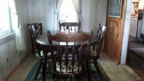 Un comedor con una mesa redonda de madera rodeada de sillas, un tapete estampado y una ventana con cortinas.