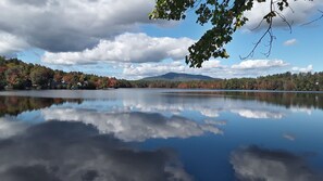 Un lago tranquilo con reflejos de árboles y nubes, rodeado de un bosque y una montaña a lo lejos.