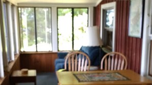 Una habitación con una mesa de comedor de madera y sillas, un sofá, y una ventana con vistas a árboles.