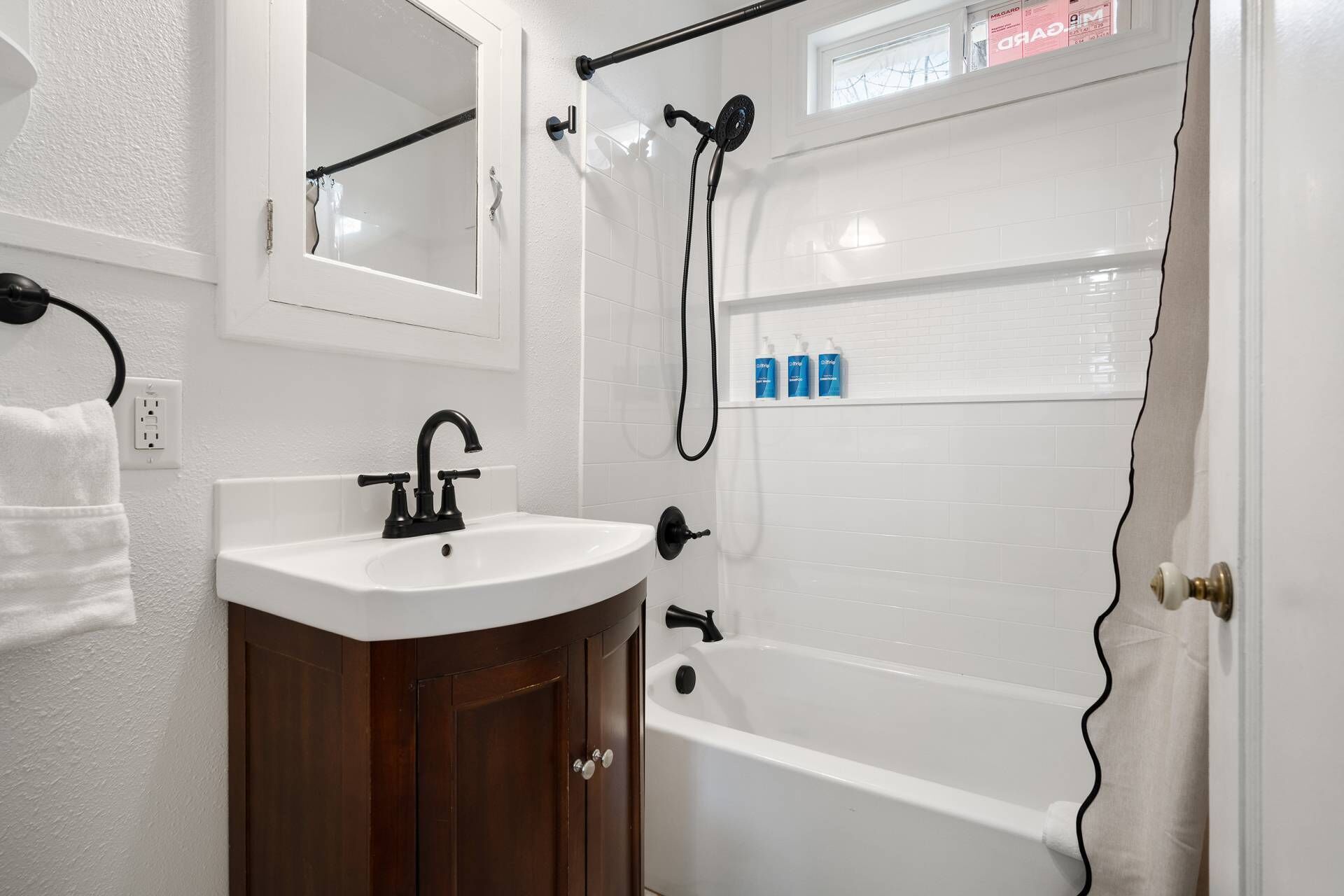 A bathroom with a white sink, dark wooden cabinet, and a white bathtub.
