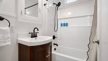 A bathroom with a white sink, dark wooden cabinet, and a white bathtub.